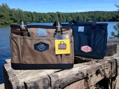 two bags sitting on top of a wooden fence next to a body of water with trees in the background