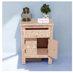 a small wooden cabinet with an ornate design painted on the front and sides, next to a potted plant