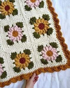 a crocheted blanket with sunflowers and leaves on it is being held by a person's hand