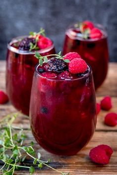 three glasses filled with raspberry sangria sitting on top of a wooden table