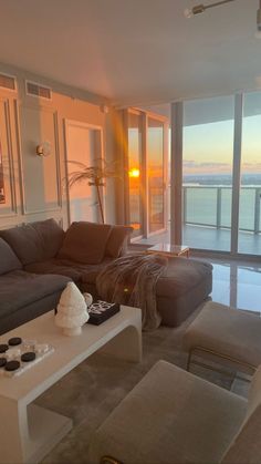 a living room filled with furniture next to large windows overlooking the ocean at sunset or sunrise