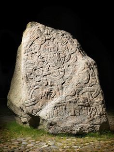 a large rock with carvings on it sitting in the middle of a grass covered field