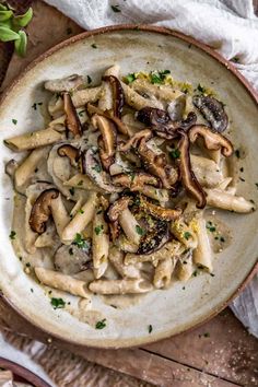 a white bowl filled with pasta and mushrooms on top of a wooden table next to utensils