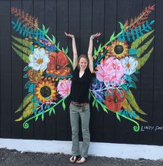 a woman standing in front of a wall with flowers painted on it's wings