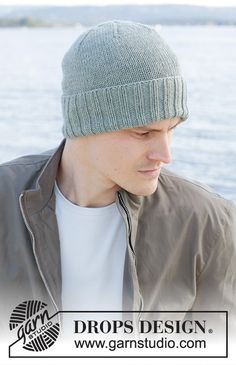 a young man wearing a green knitted hat next to the water with an island in the background