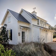 a white house with a black roof and two garages on the side of it