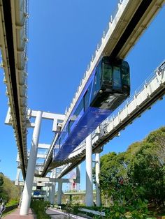 a blue and white train traveling over a bridge next to lush green trees on a sunny day