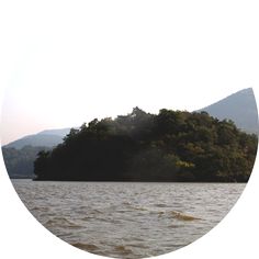 an island in the middle of a lake surrounded by trees and hills with sun shining through