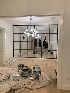 an empty room with some paint cans on the floor and a chandelier in the background