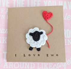 a card with a crocheted sheep holding a red heart on it's side