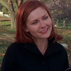 a woman with red hair is smiling at the camera while standing in front of some trees