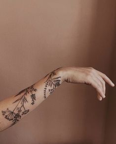 a woman's arm with flowers and leaves on it, in front of a brown wall