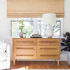 a white couch sitting next to a wooden dresser in a living room under a window