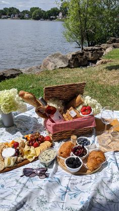 a picnic with bread, fruit and cheeses on the grass next to a lake