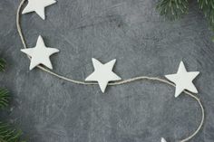 three white stars are hanging from a string on a gray surface with pine branches around them