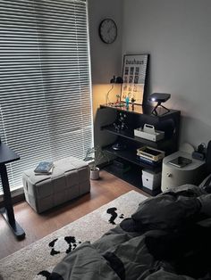 a bedroom with a bed, desk and window covered in blinds on the windowsill