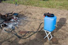 a blue tank sitting on top of a metal stand next to a campfire with a hose