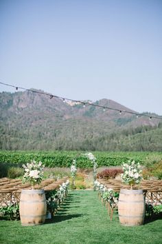 an outdoor ceremony set up with wooden barrels and white flowers on the grass in front of mountains