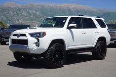 a white toyota 4runner is parked in a parking lot with mountains in the background