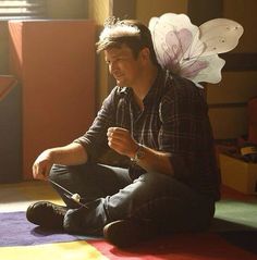 a man is sitting on the floor with paper flowers in his hair and holding a cell phone