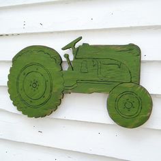 a green wooden toy tractor hanging on the side of a white house with wood siding