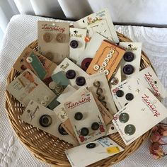 a basket filled with lots of different types of buttons and paper on top of a bed