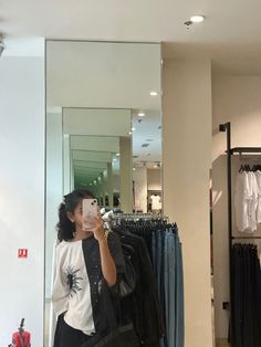 a woman taking a selfie in front of a mirror with clothes on hangers