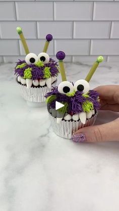 two cupcakes with googly eyes and purple flowers on them are being held by someone's hand