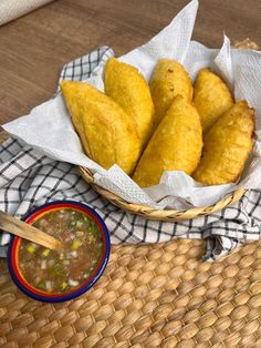 a basket filled with fried food next to a bowl of soup and dipping sauce on a table