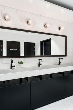 a bathroom with two sinks, mirrors and lights on the wall above them is shown