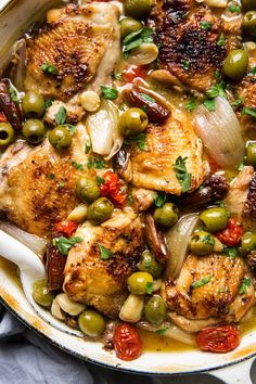 a skillet filled with chicken, olives and tomatoes on top of a table