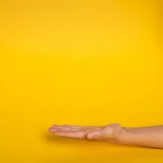 a person's hand reaching out towards an orange object on a yellow background with copy space