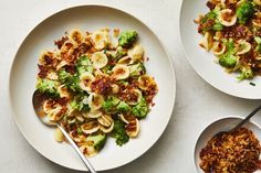 two plates of pasta with broccoli and other food on the table next to each other