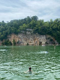 a person swimming in the middle of a lake near a rocky cliff and some trees