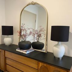 a dresser with two vases and a mirror on top of it next to a lamp