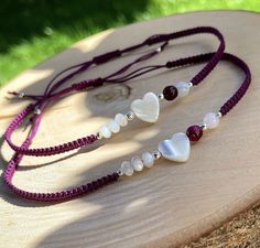 two necklaces with hearts and beads on a piece of wood in front of grass