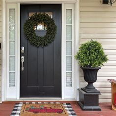 a black front door with a wreath on it and two potted plants next to it