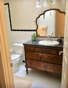 a white toilet sitting next to a bathroom sink under a mirror on top of a wooden cabinet