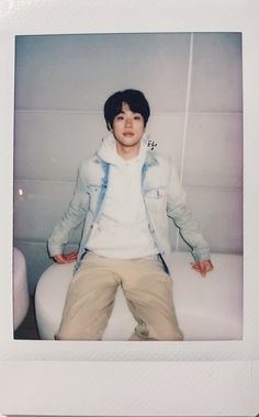 a young man sitting on top of a white couch next to a wall and holding his hands in his pockets