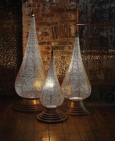 three lamps sitting on top of a wooden floor in front of a brick wall with light coming from them