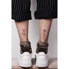 the legs and ankles of a person wearing white sneakers with flowers tattooed on their feet