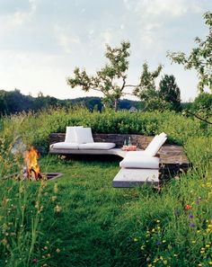 a fire pit in the middle of a field with two lounge chairs and an open fire