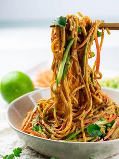 a white bowl filled with noodles, carrots and cilantro on top of a table