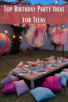 an outdoor birthday party with balloons and plates on the table, surrounded by pink and blue pillows