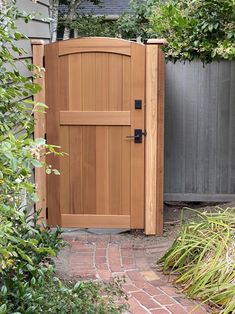 a wooden gate in the middle of a brick path next to a fence and shrubbery