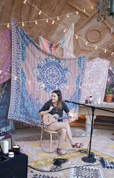 a woman sitting in a chair playing an acoustic guitar on stage with lights strung above her