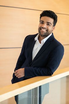 a smiling man in a suit leaning on a railing