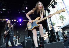 two women are playing guitars on stage at an outdoor music festival in front of a crowd