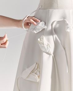 a woman is tying a white ribbon to a dress with flowers on the back and side