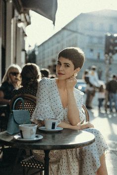 a woman sitting at a table with a cup of coffee in front of her on the street